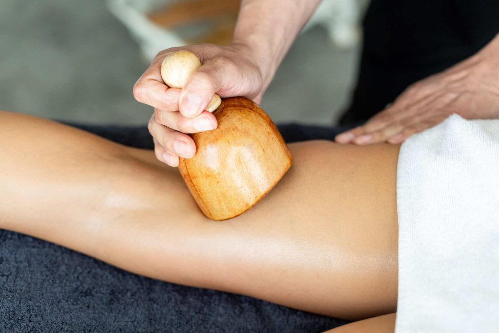 Masaje de maderoterapia en piernas con copa de madera para reducir celulitis.